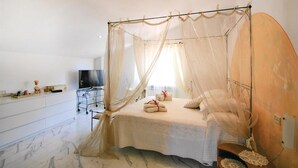 A bedroom with a four-poster canopy bed, a television, a vanity with a mirror, and a marble floor.