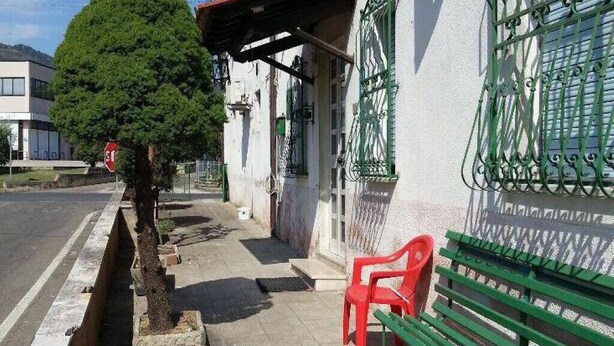 A sidewalk with a bench, a tree, and a building with green metal gates. - Holiday home in Val di Chiana (Castiglion Fiorentino)