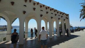 Ein überdachter Gang mit Bögen, Blumentöpfen und Blick aufs Meer.