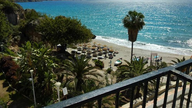 Ein Strand mit Sonnenschirmen und Liegestühlen, eine Palme und Blick auf den Ozean und die Berge.
