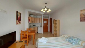 Ein kleines Zimmer mit Bett, Schreibtisch, Fernseher und Küchenzeile.