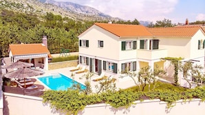 Une maison à deux étages avec une piscine, des volets verts et une vue sur les montagnes en arrière-plan.