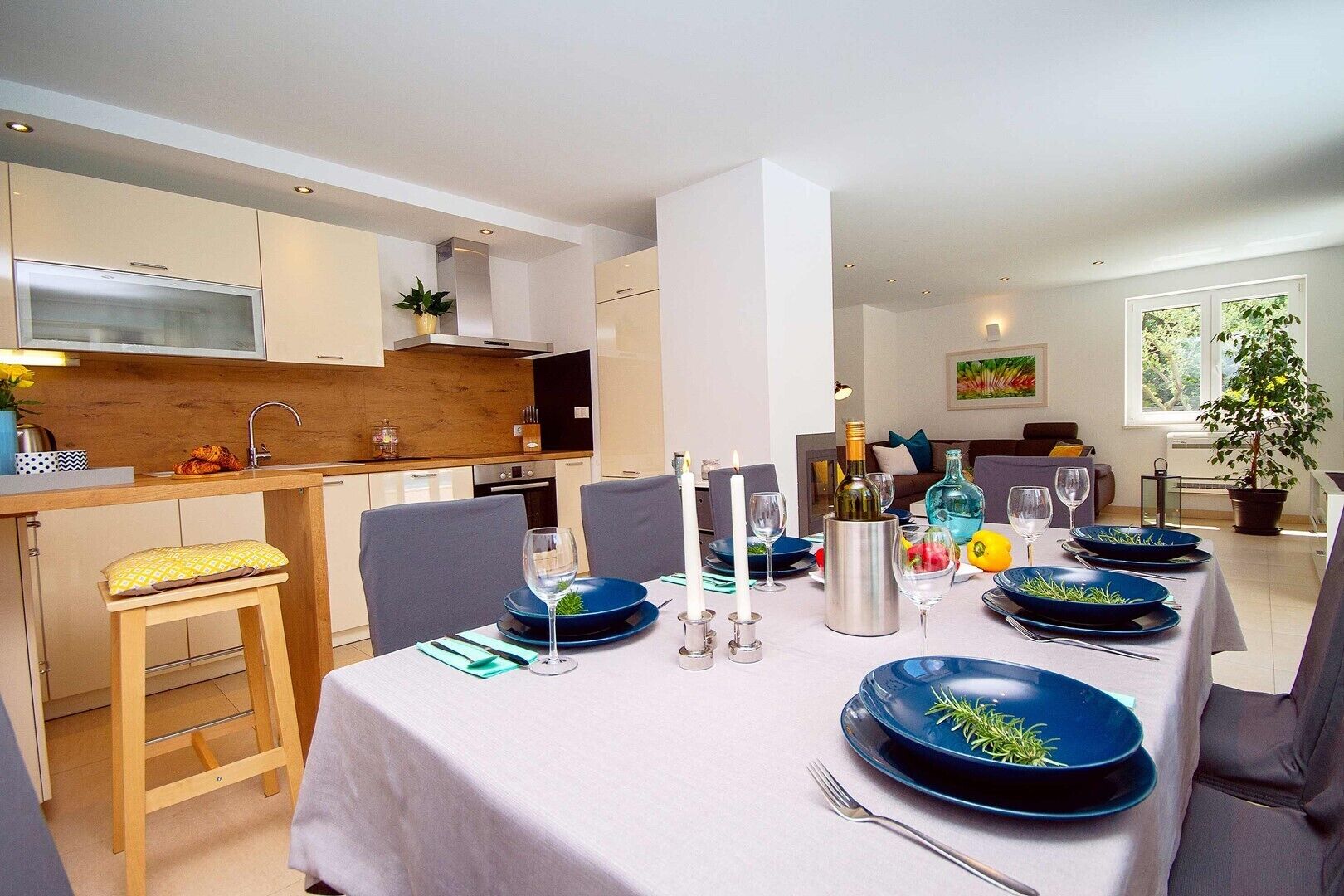 A modern dining area with a table set for four, featuring blue plates and candles.