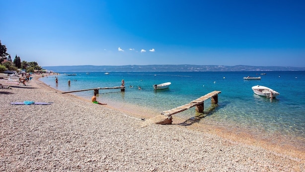 Une plage de galets, avec des bateaux et un ciel bleu dégagé.