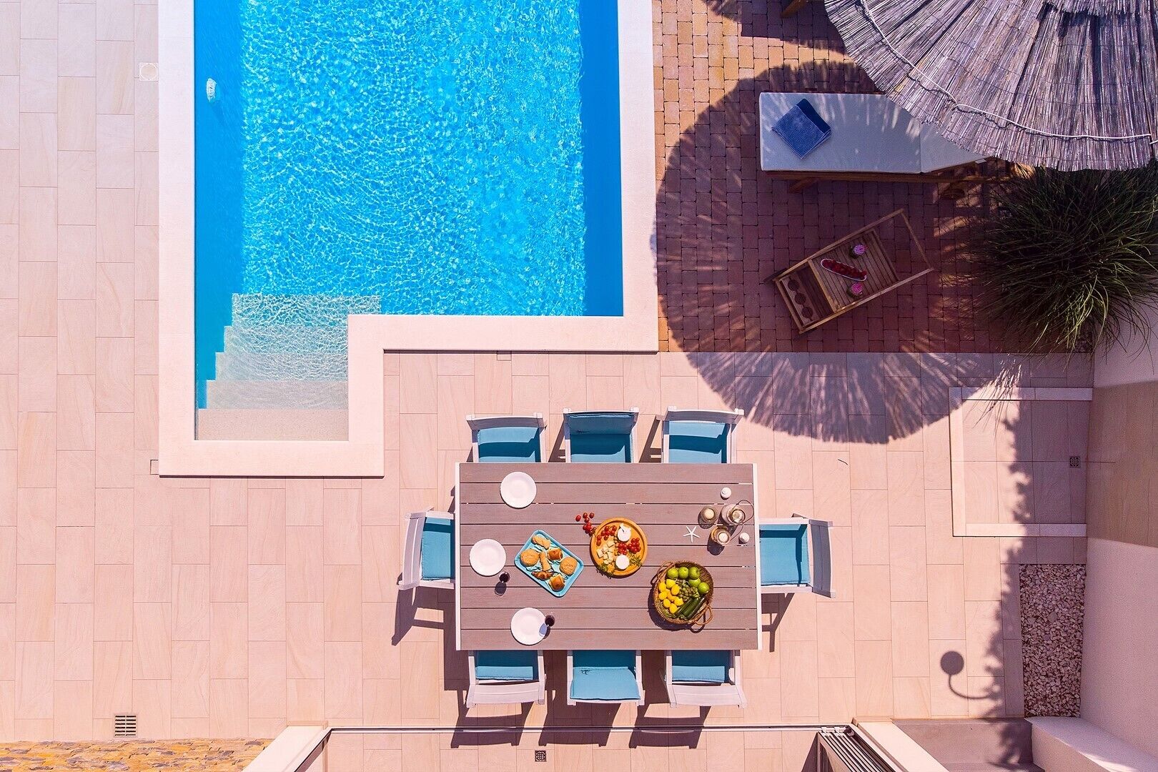 Un espace piscine extérieur avec une table et des chaises, entouré d’une terrasse carrelée.