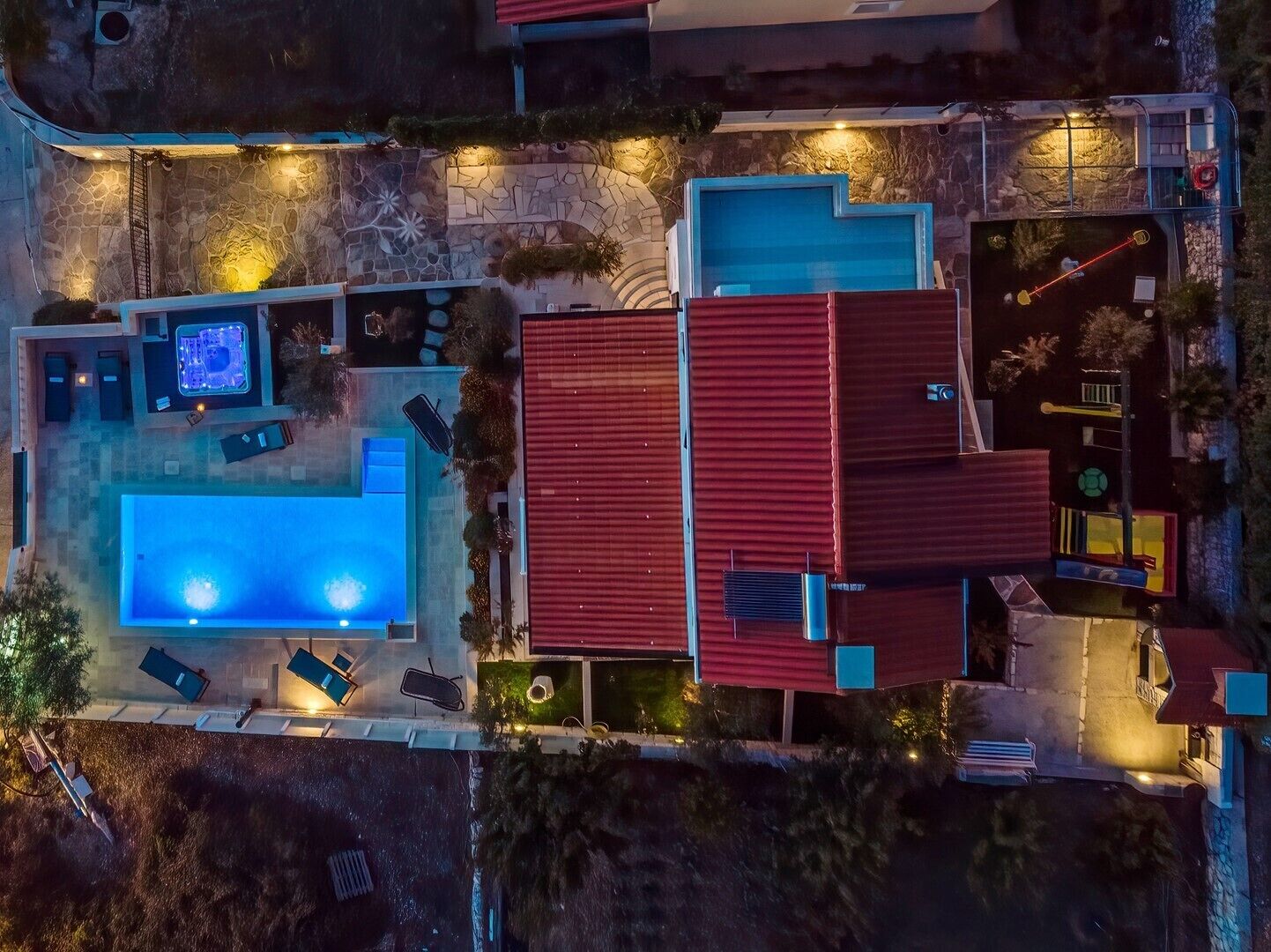 An aerial view of a property with a swimming pool, outdoor seating, and a red-roofed building.