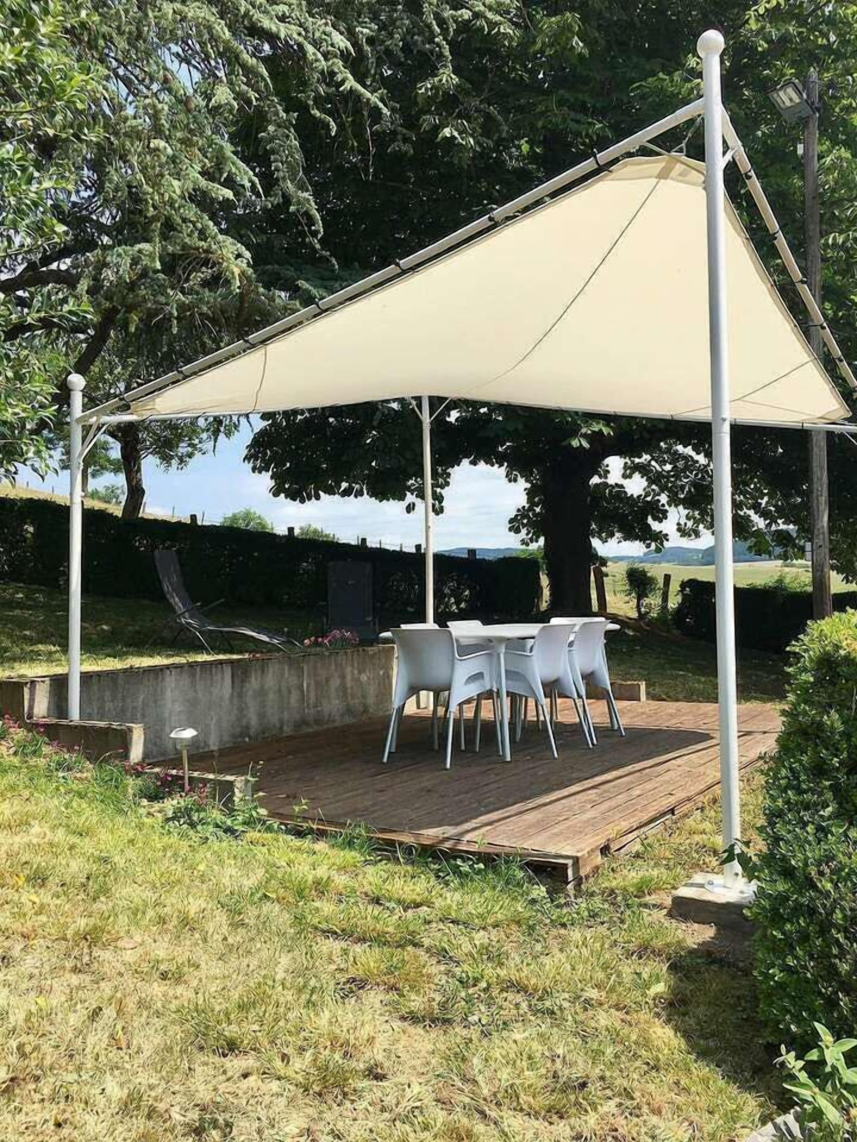 Een overdekt terras met een tafel en stoelen, omgeven door groen en bomen.