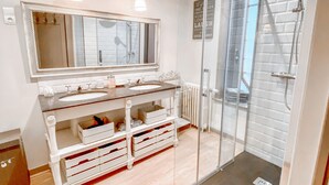 A modern bathroom with a glass-enclosed shower, a large mirror, and a vanity with drawers.