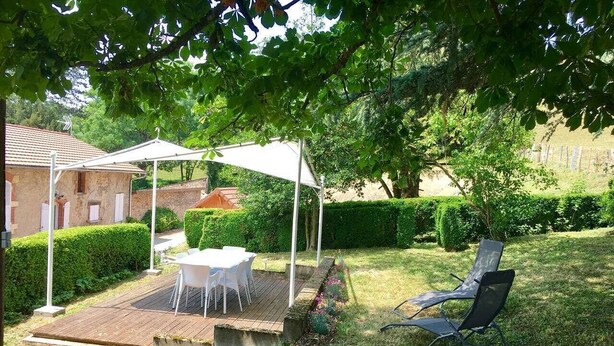 A patio with a table and chairs under a white canopy, surrounded by a well-maintained garden and a hedge.