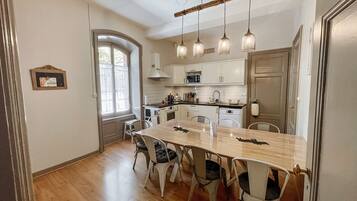 A kitchen with white cabinets, a wooden dining table, and hanging pendant lights.