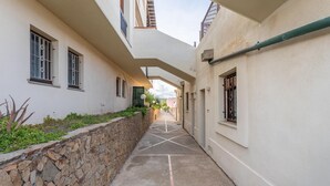Un estrecho callejón con paredes de piedra y ventanas, que conduce a un edificio con techo plano y una tubería visible.