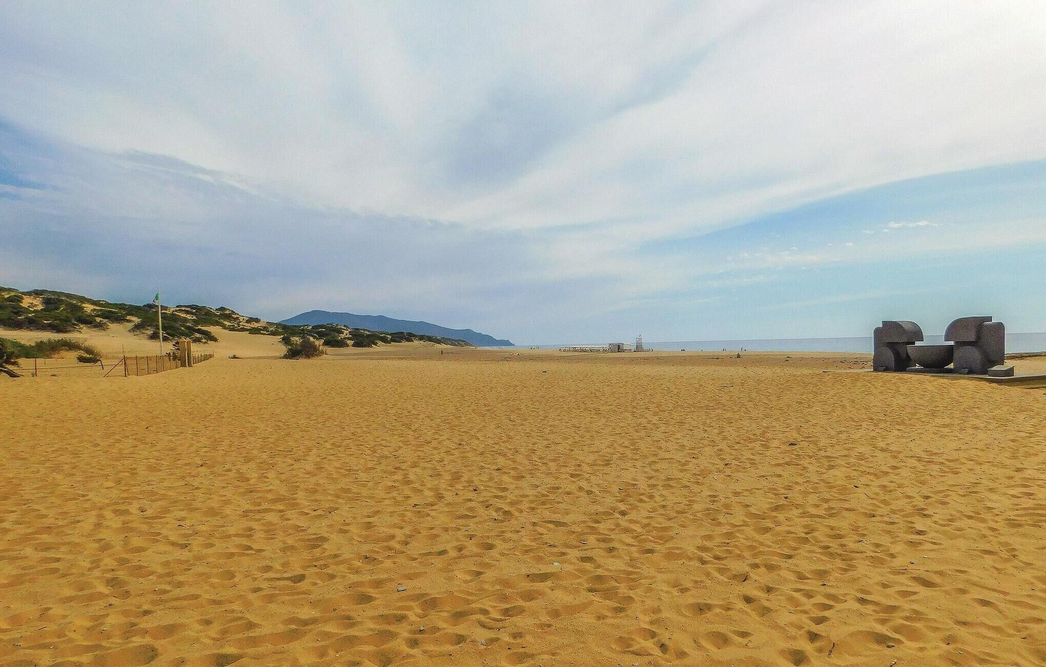 Una amplia playa de arena con algunas construcciones y un cielo despejado.