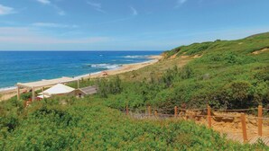Un paisaje costero con una playa, un edificio de techo blanco y un área ajardinada cercada.