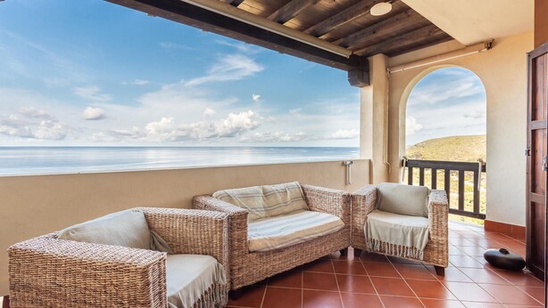 Un espacio de estar al aire libre cubierto con muebles de mimbre y vista al océano.