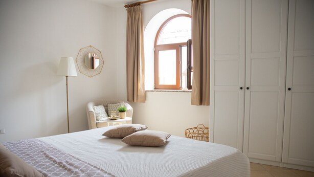 Een slaapkamer met een groot bed, een stoel met een plant, een lamp en een kledingkast.