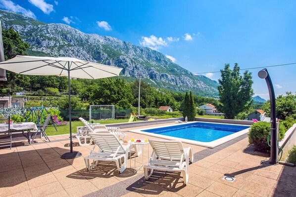 Ein Poolbereich mit Blick auf Berge, Sitzmöglichkeiten im Freien und einem Tisch mit Getränken.