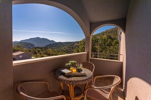 Ein Balkon mit Korbstühlen, einem kleinen Tisch und Blick auf eine Berglandschaft.