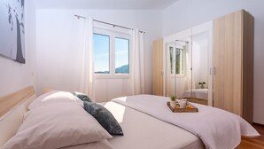 A bedroom with a bed, a bedside table, a mirror, and a window with curtains.