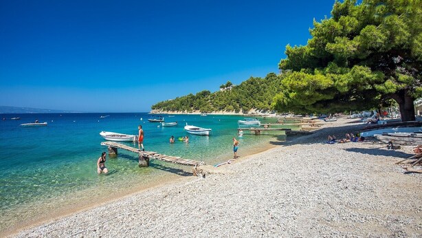 A beach with clear turquoise water, boats, and people.