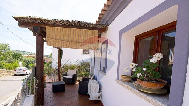Eine überdachte Terrasse mit Gartenmöbeln, einem Fernseher und Topfpflanzen.