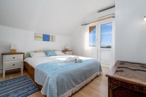 Ein Schlafzimmer mit Bett, zwei Nachttischen, einem Fenster mit Vorhängen und Blick zum Himmel.