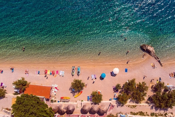 Eine Luftaufnahme eines Strandes mit klarem türkisblauem Wasser, Sonnenschirmen und Liegestühlen.