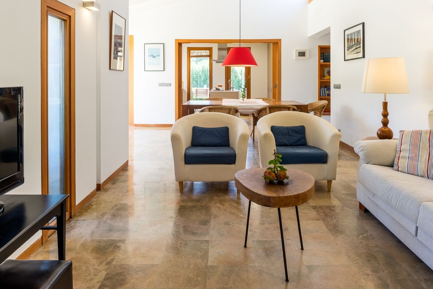 A modern living room with a TV, two sofas, a coffee table, and a dining area with a red lamp.