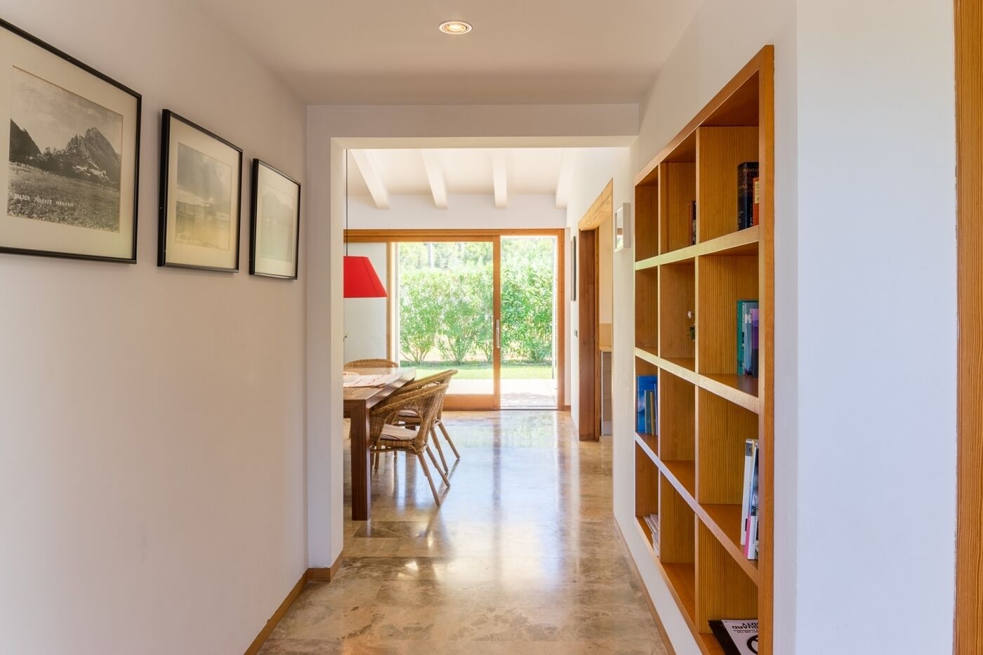 A hallway with a dining area, wooden bookshelves, and framed pictures on the walls.