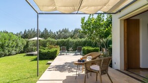 Une terrasse extérieure avec une table et des chaises, un espace abrité et une vue sur un jardin et des arbres.