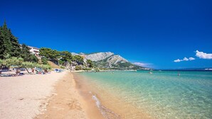 Een strand met helder turquoise water, een zandstrand en een bergachtige achtergrond.