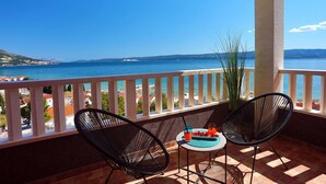 Een balkon met twee stoelen en een kleine tafel, met uitzicht op de kust onder een heldere lucht.