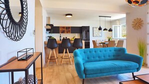 Een moderne woonkamer met een blauwe bank, een houten salontafel en een keuken op de achtergrond.