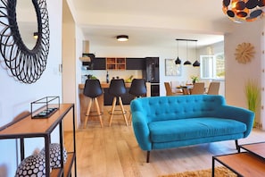 Un salon moderne avec un canapé bleu, une table basse en bois et un coin cuisine à l’arrière-plan.