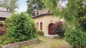 A house with a stone pathway leading to a wooden door, surrounded by lush greenery and a stone wall.