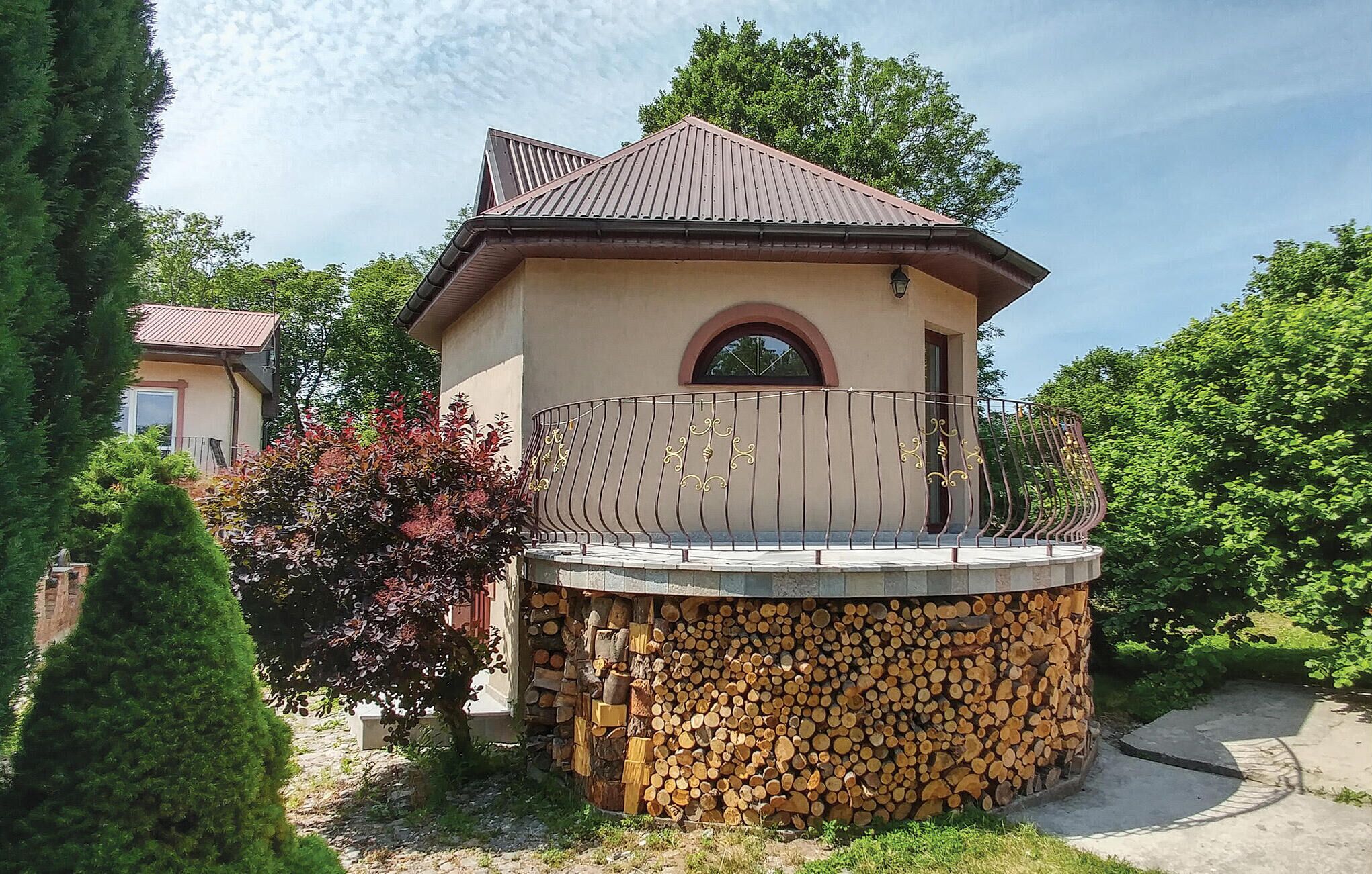Une maison avec un mur circulaire fait de rondins de bois, un balcon doté d’une rambarde en métal et un toit rouge.