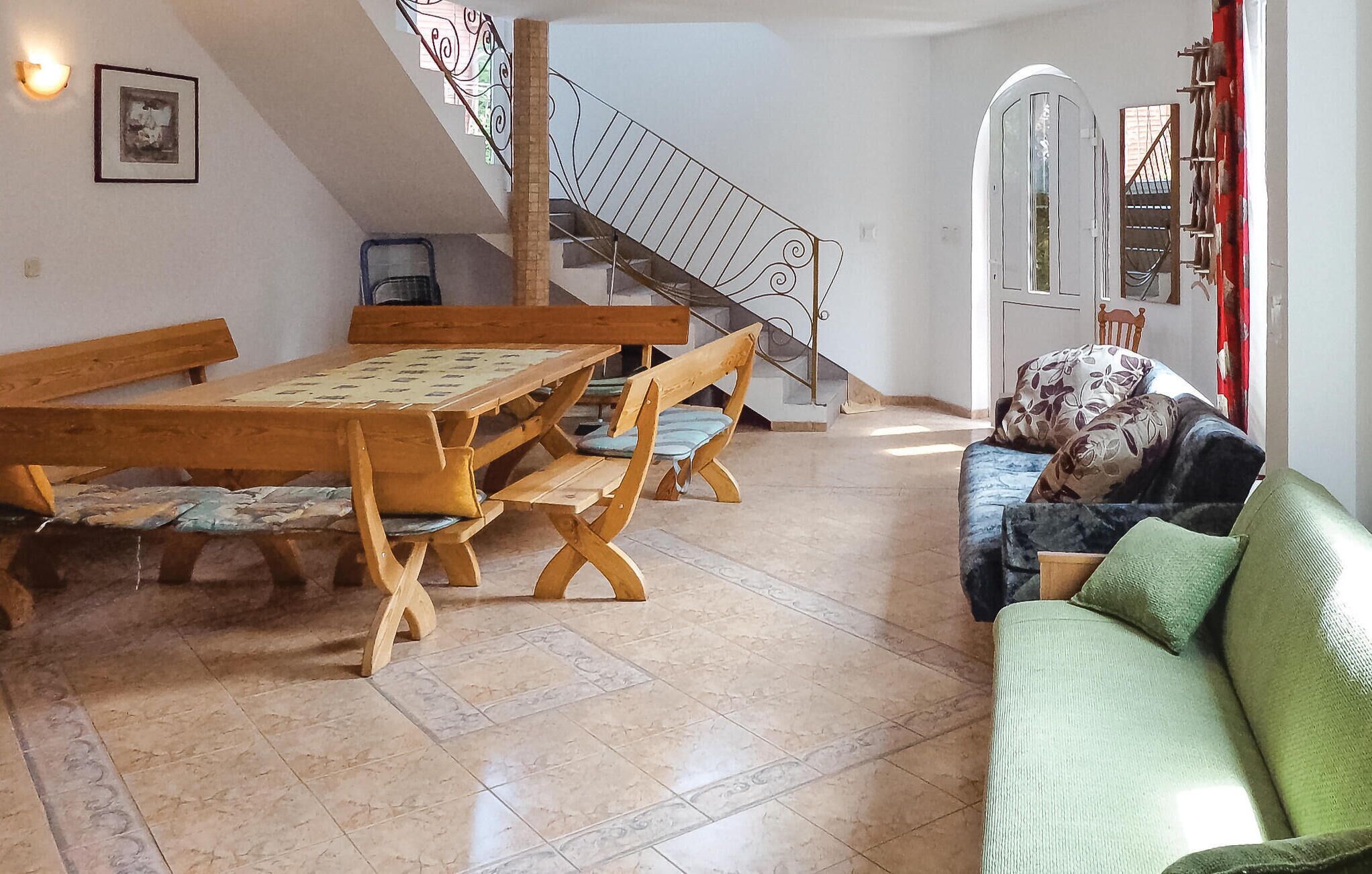 Un área de comedor con una mesa de madera y bancos, una escalera con barandilla metálica, y un sofá con cojines estampados.