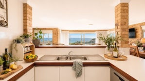 A kitchen with a view of the sea, a brick wall, and a wooden countertop. - Absolute Beachfront Escape · Ocean Views · Family Luxury (Halls Head)