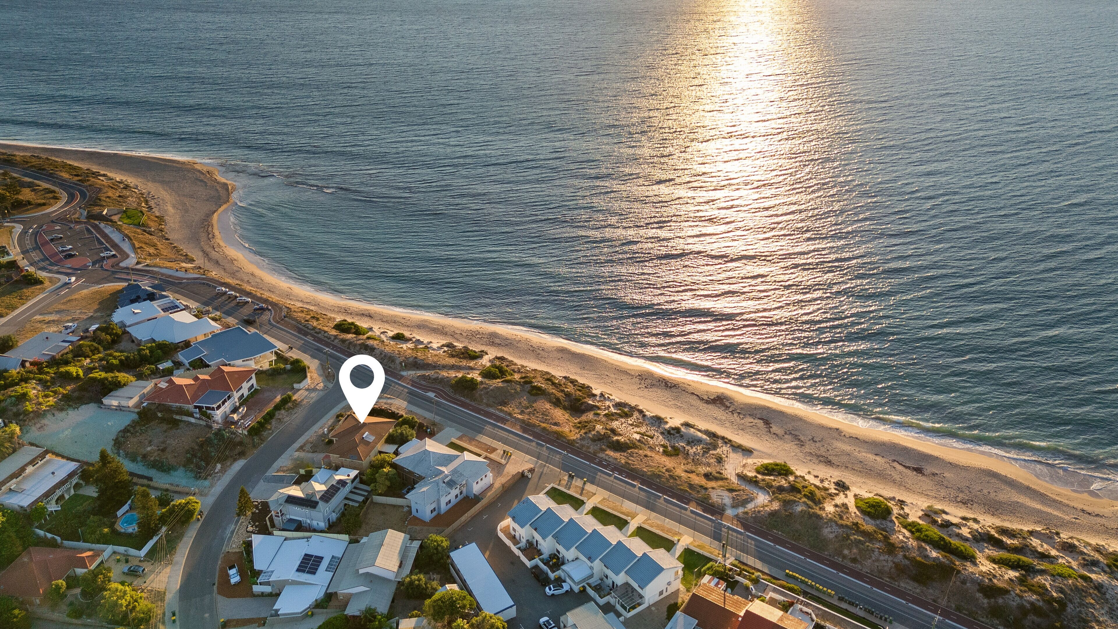 An aerial view of a coastal area with a beach, roads, and residential buildings.