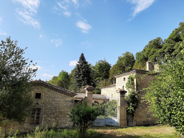 Un bâtiment rustique en pierre, doté d’un toit en tuiles, entouré d’une végétation luxuriante et d’arbres.