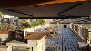 Un patio al aire libre con terraza de madera, paredes de piedra y techo de tejas.