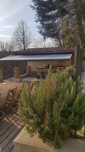 A patio area with a wooden table and chairs, a stone bench, and a small potted plant. - Pool house 10 people Crest, Saou Valence (Divajeu)