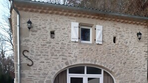 Un edificio de piedra con un amplio arco de entrada, una pequeña ventana con contraventanas y una letra 'S' en la pared.