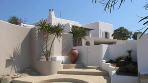 Un edificio moderno con fachada blanca, un jarrón grande y palmeras.