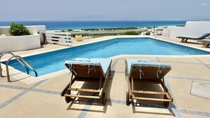 Un área de piscina con dos sillas de descanso, una piscina y vistas al mar.