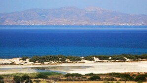 Un paisaje costero con una playa, vegetación y montañas lejanas.