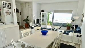 Una cocina moderna con armarios blancos, una mesa de comedor con sillas, un tazón azul y vistas al exterior a través de una puerta abierta.
