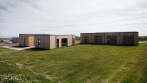 Dos edificios modernos con amplias ventanas y un campo verde al frente.