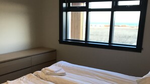 Una habitación con dos camas, una ventana con persianas, una mesita de noche y vistas a la playa.