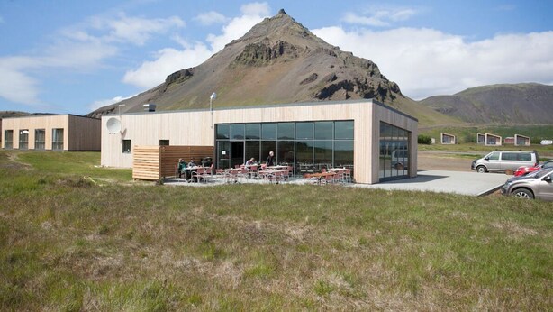 Un edificio moderno con fachada de vidrio, zona de estar al aire libre y montañas al fondo.