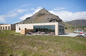 A modern building with a glass facade, outdoor seating area, and a mountain backdrop. - Fell Holiday Home (Arnarstapi)